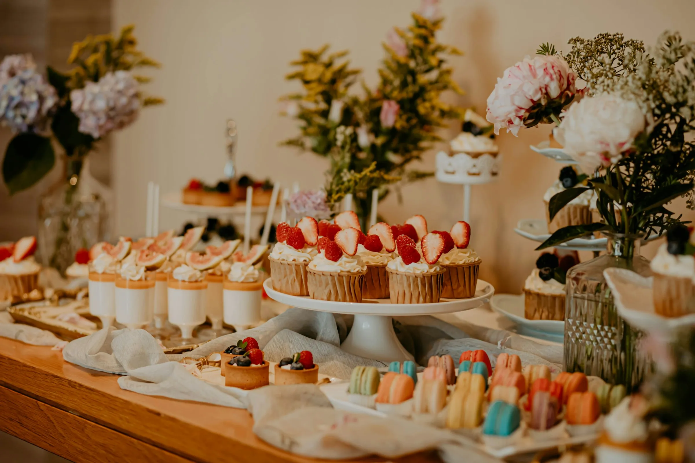 A dessert table with strawberry cupcakes, macarons and fresh flowers