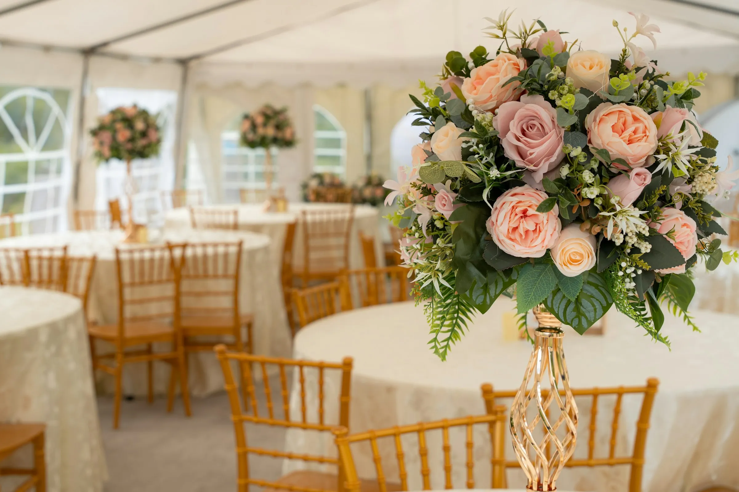 A rose centrepiece above round tables dressed in linen